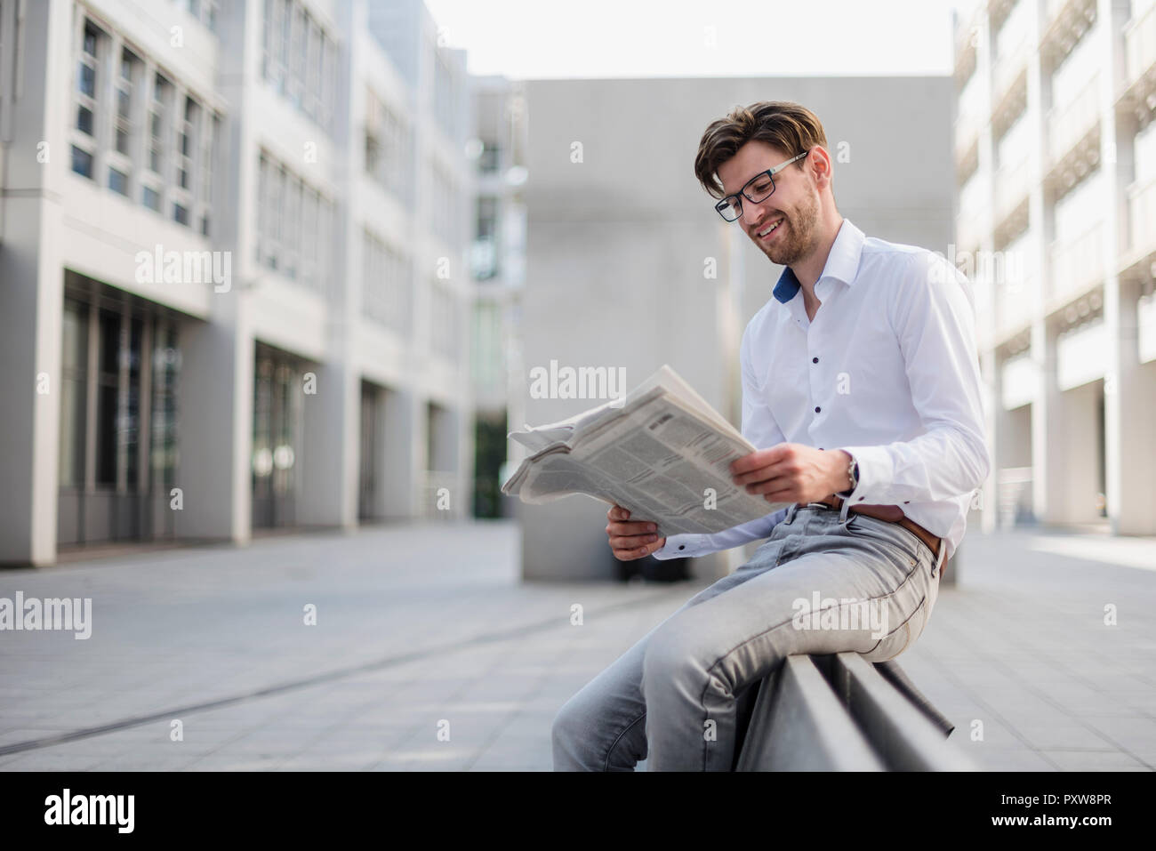 Smiling businessman sitting in the city reading newspaper Stock Photo
