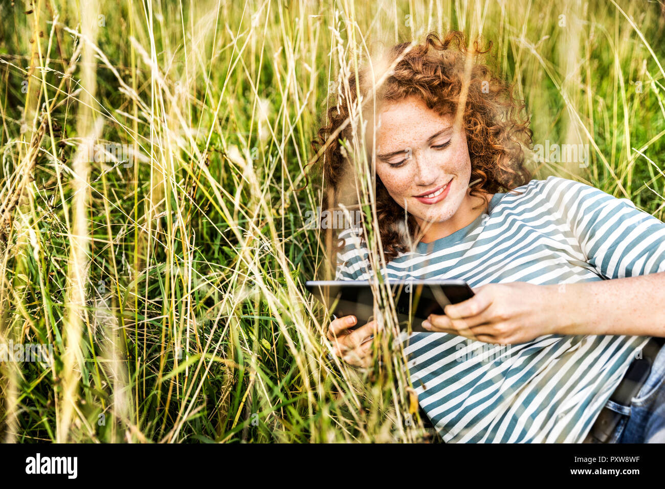 Smiling young woman relaxing on a meadow with tablet Stock Photo