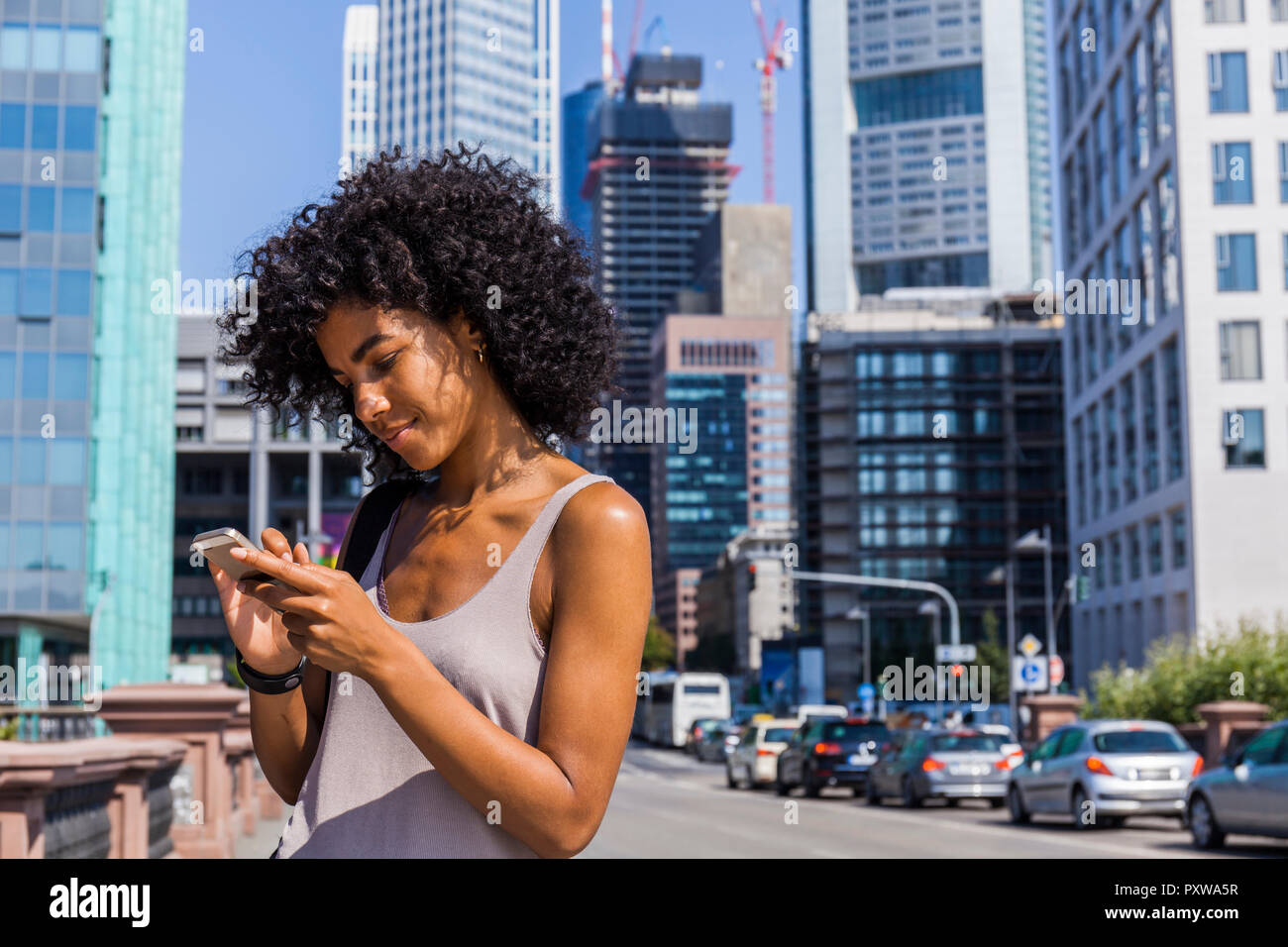 Germany, Frankfurt, young woman with curly hair using cell phone Stock Photo