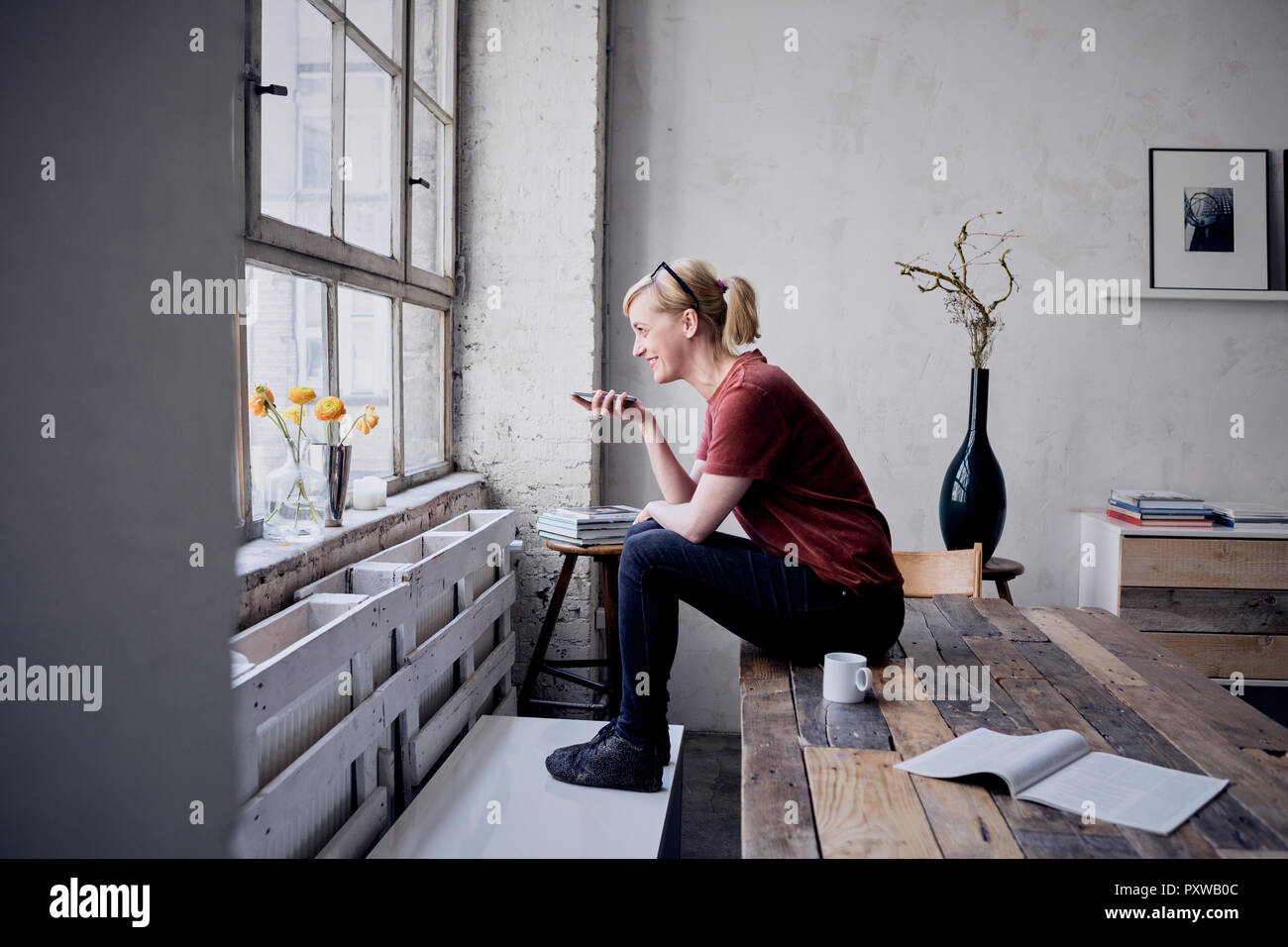 Woman sitting on desk in loft using cell phone Stock Photo