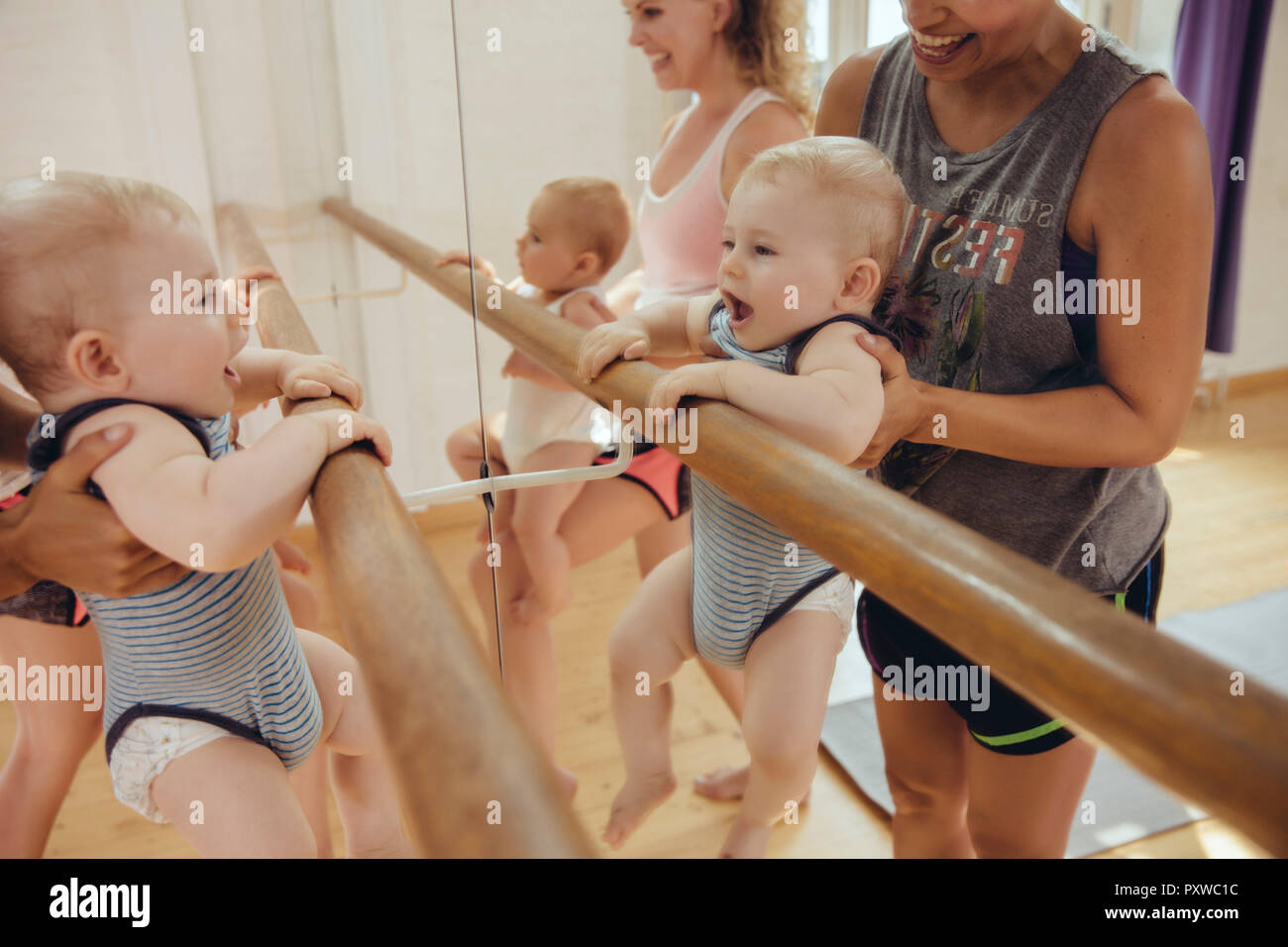 Two mothers holding up their small children to barre in dance studio Stock Photo