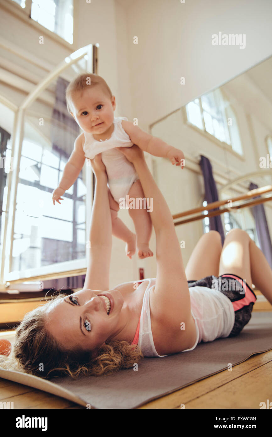 Mother working out on yoga mat while holding up her baby Stock Photo