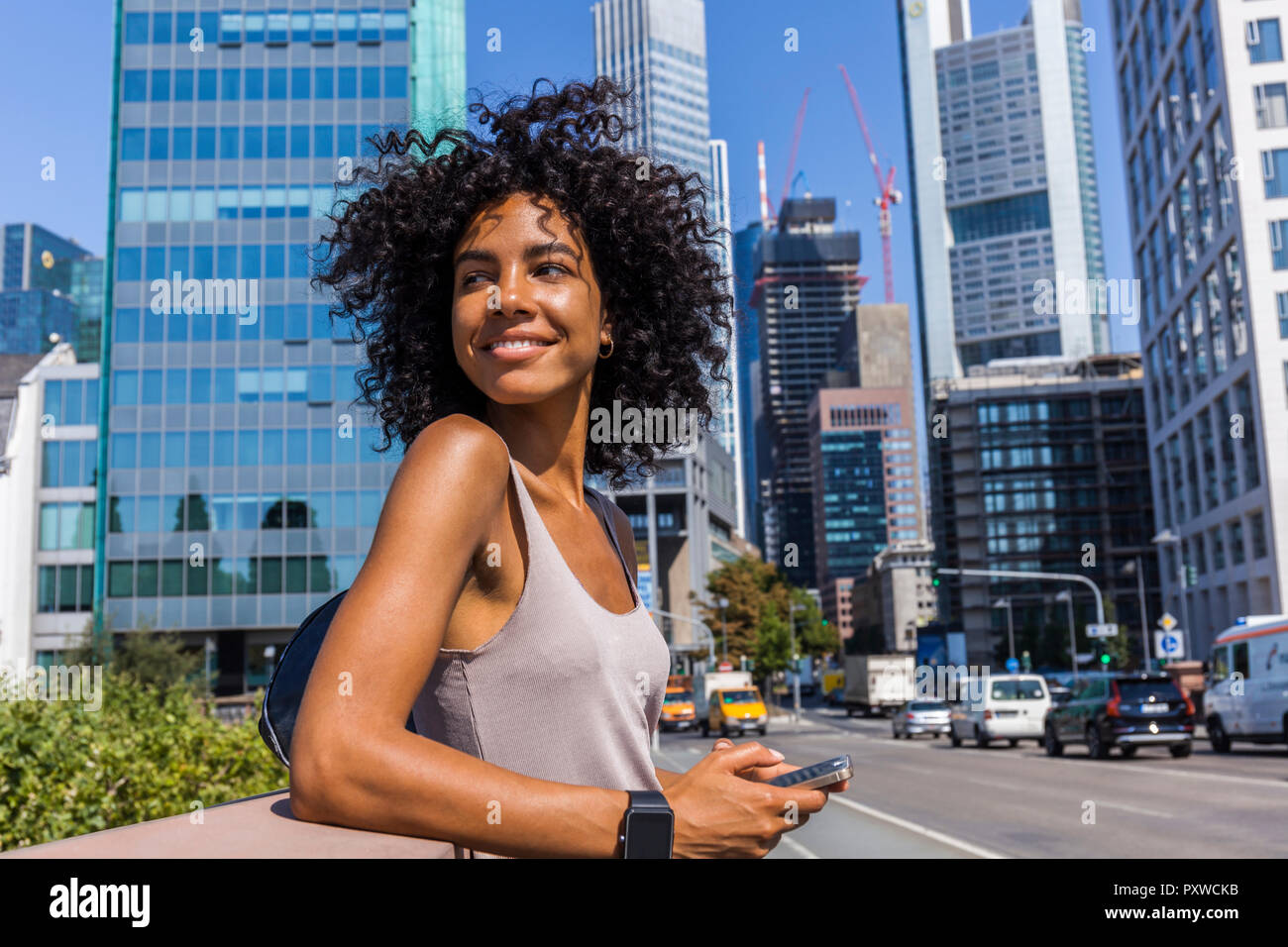 Germany, Frankfurt, portrait of smiling young woman with curly hair in the city Stock Photo