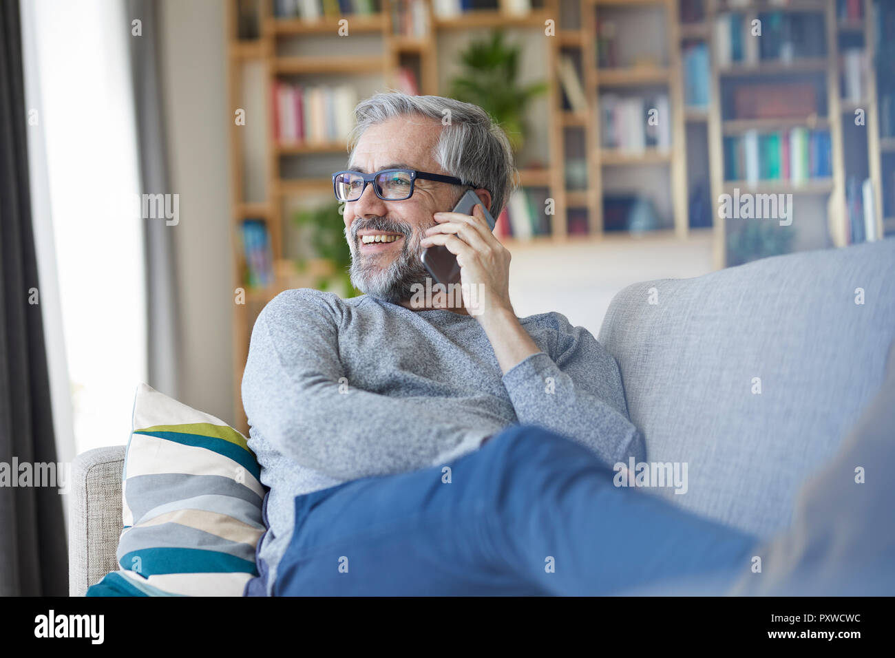 Mature man on the phone sitting on couch at home looking out of window Stock Photo
