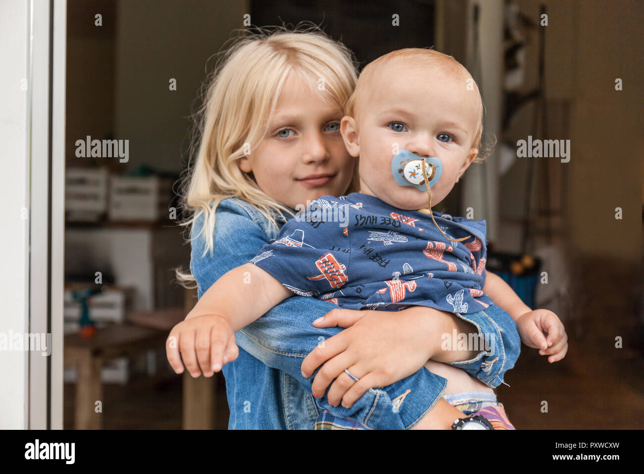 Portrait of girl holding baby boy brother at home Stock Photo