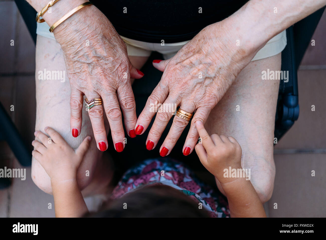 Hand of baby girl pointing on hand of senior woman with rings and red painted nails Stock Photo