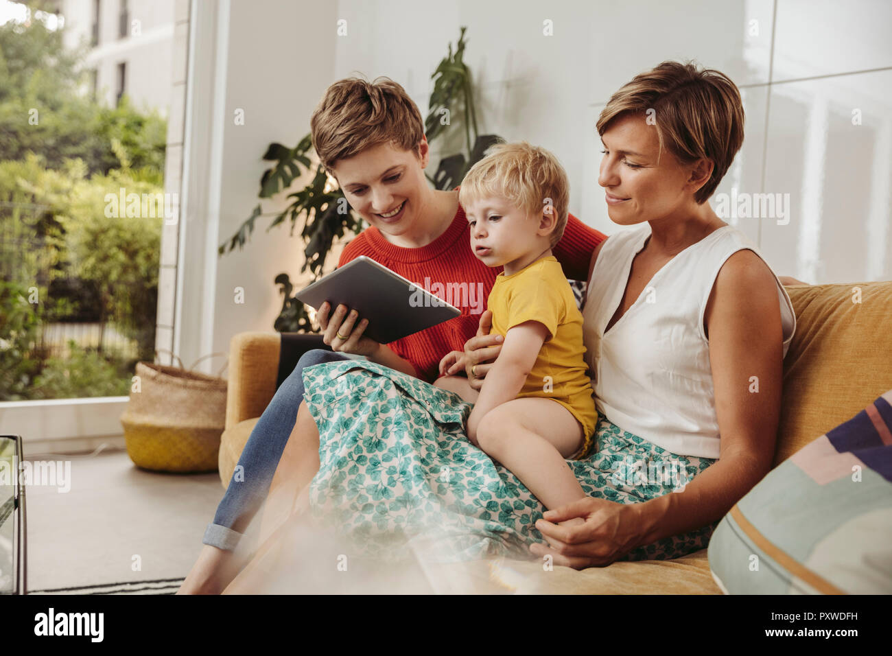 Two mothers looking at a tablet computer with their child at home Stock Photo