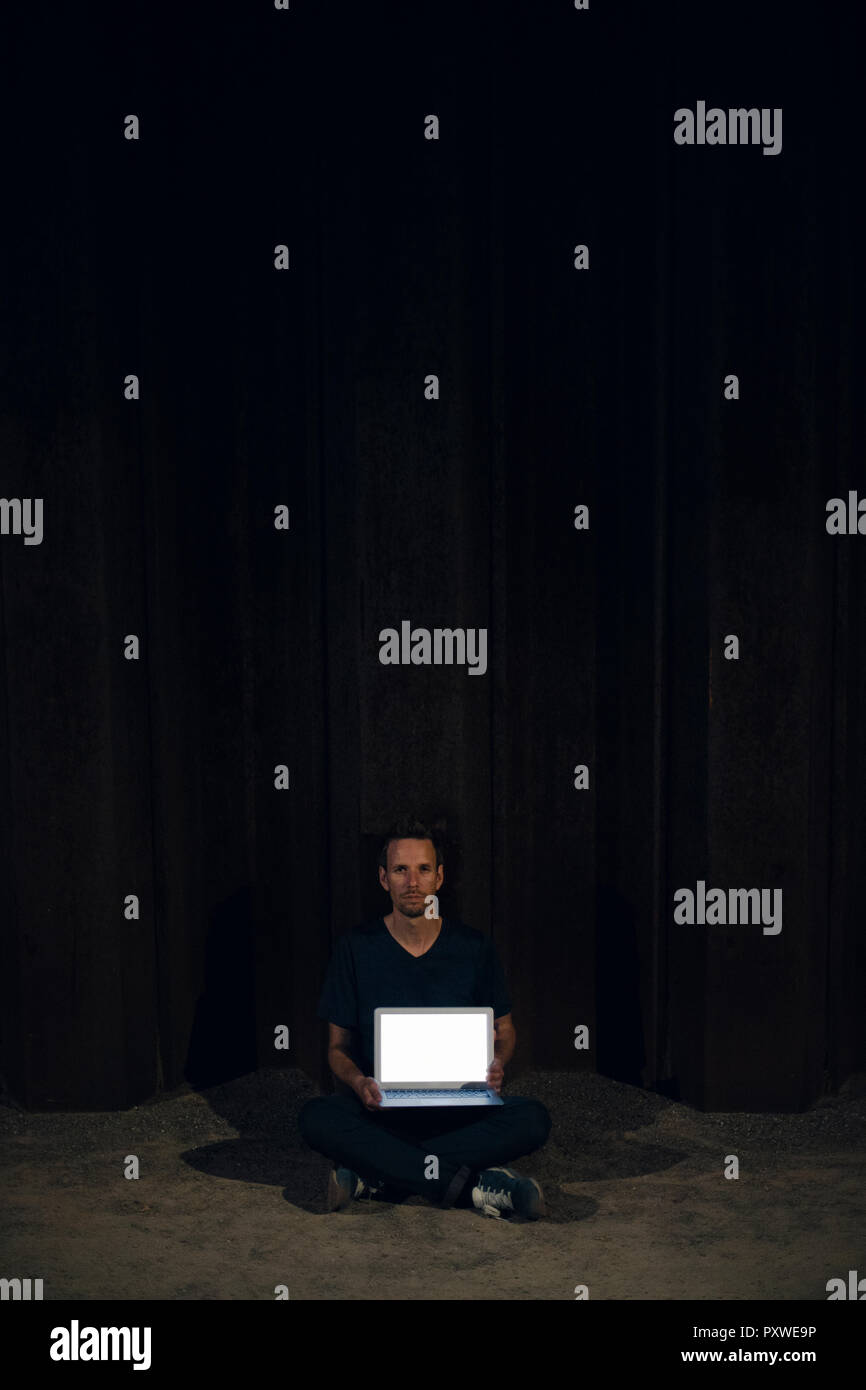 Mid adult man sitting cross-legged on ground, showing blank laptop screen Stock Photo