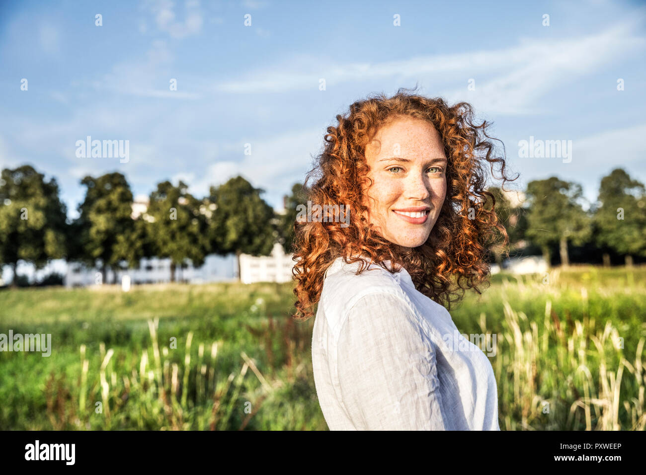 Germany, Cologne, portrait of smiling young woman with curly red hair in nature Stock Photo