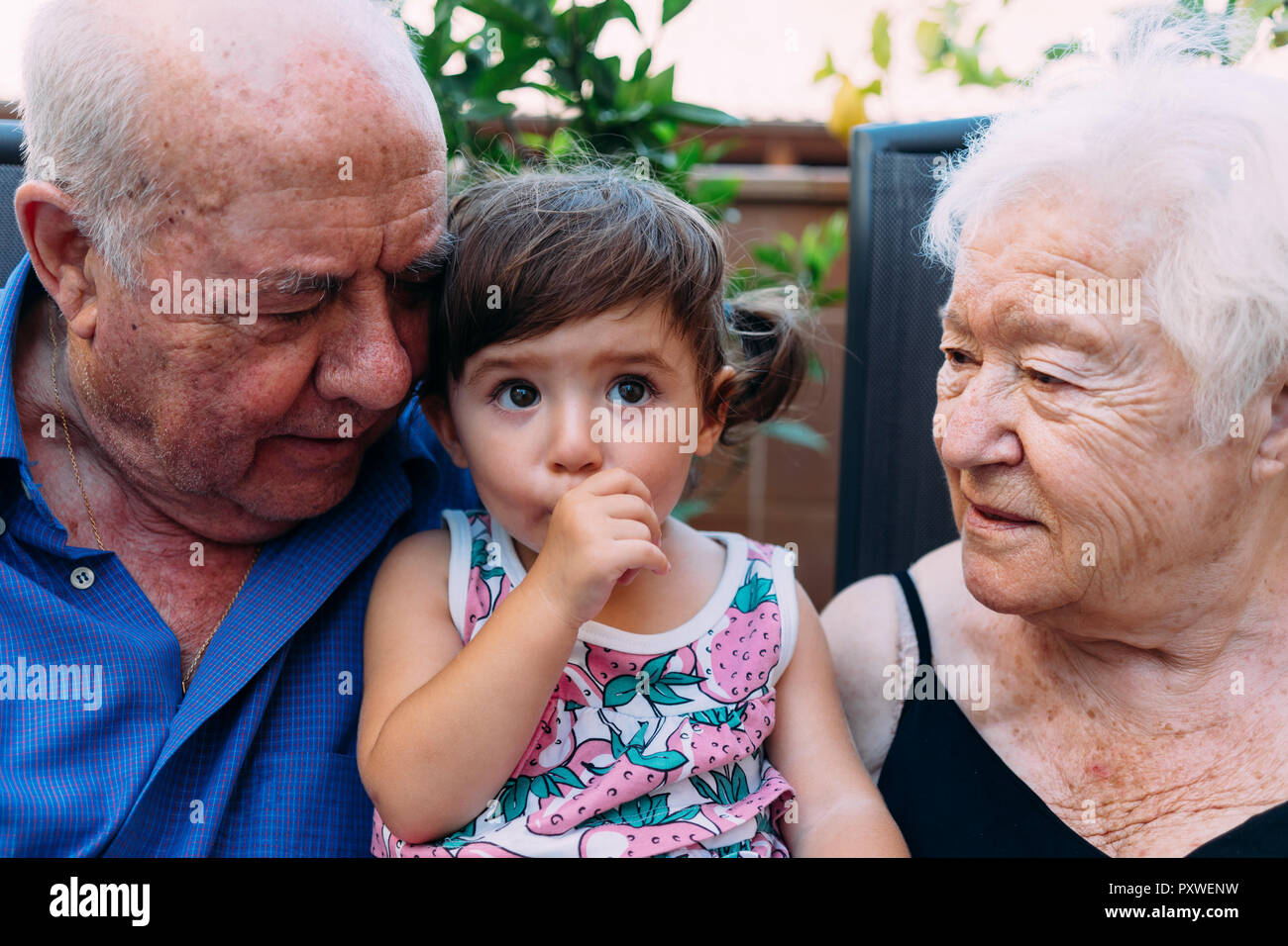 Grandparents looking at baby girl sucking thumb Stock Photo