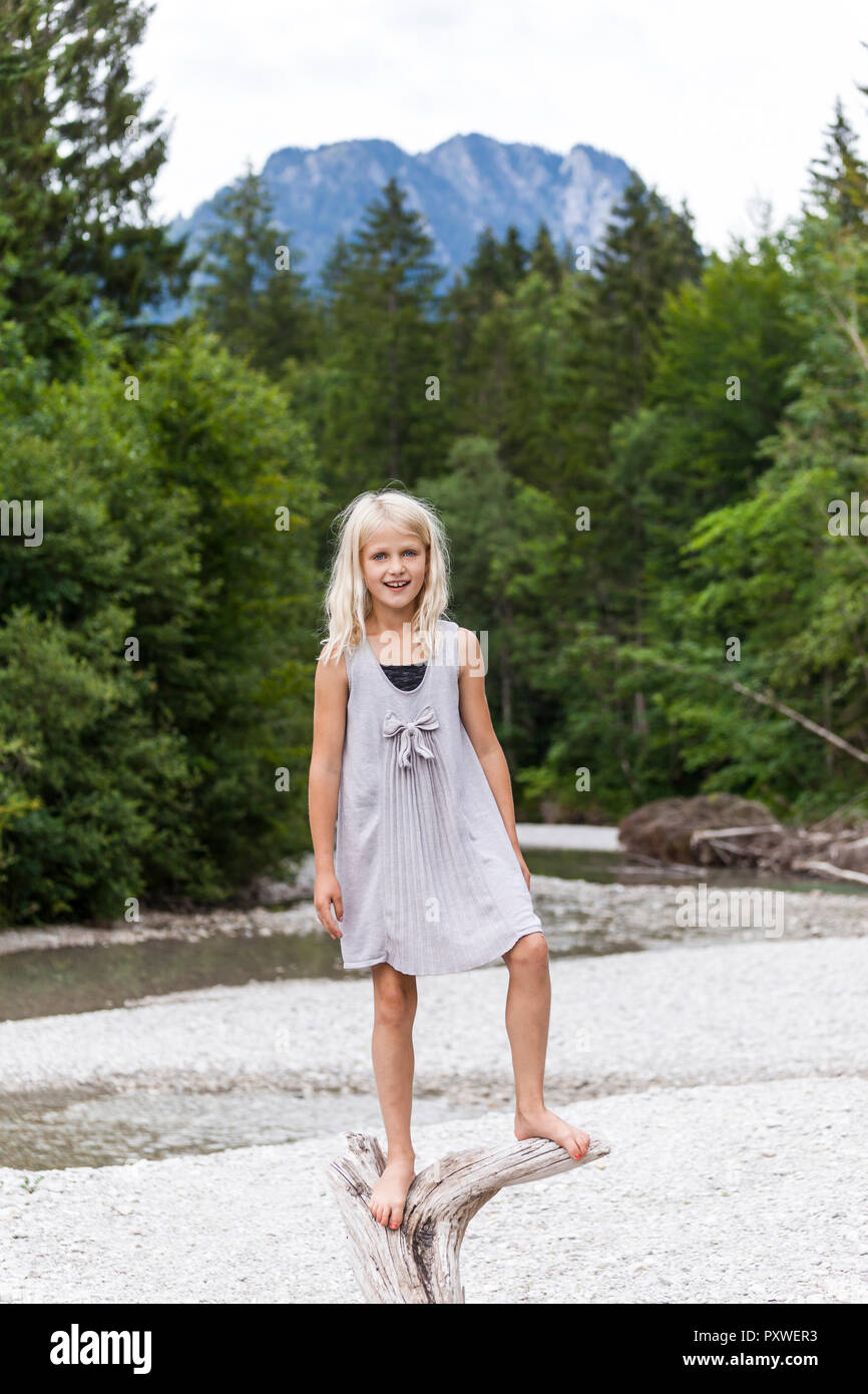 Portrait of smiling girl standing on dead wood at the riverside Stock Photo