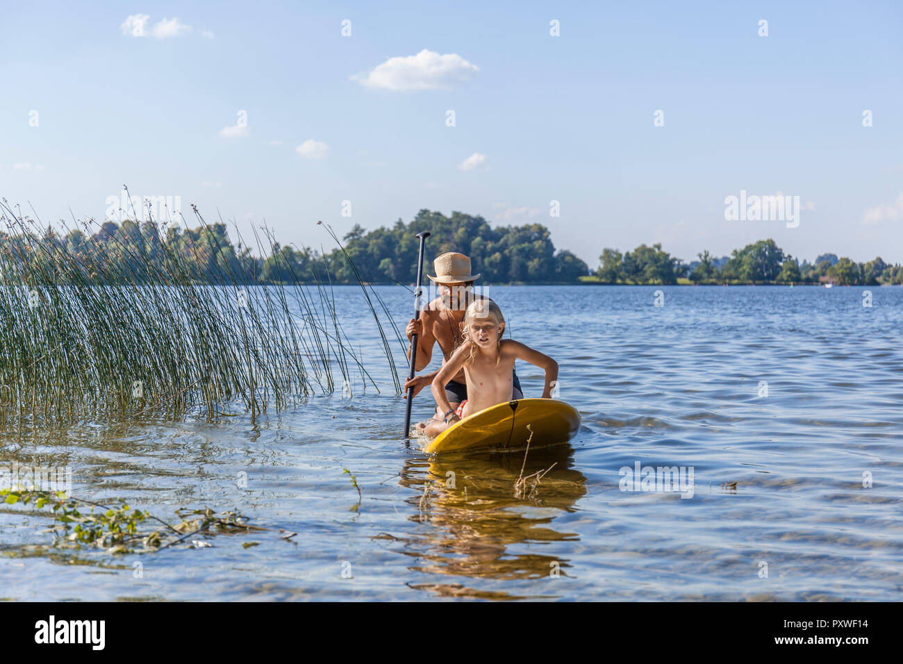 Father and daughter paddle boarding on lake Stock Photo