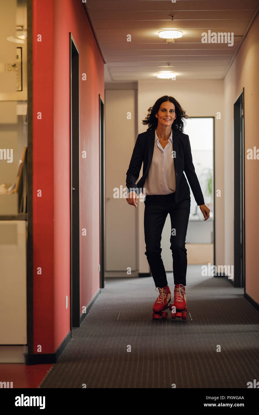 Mature businesswoman rollerskating in office corridor Stock Photo