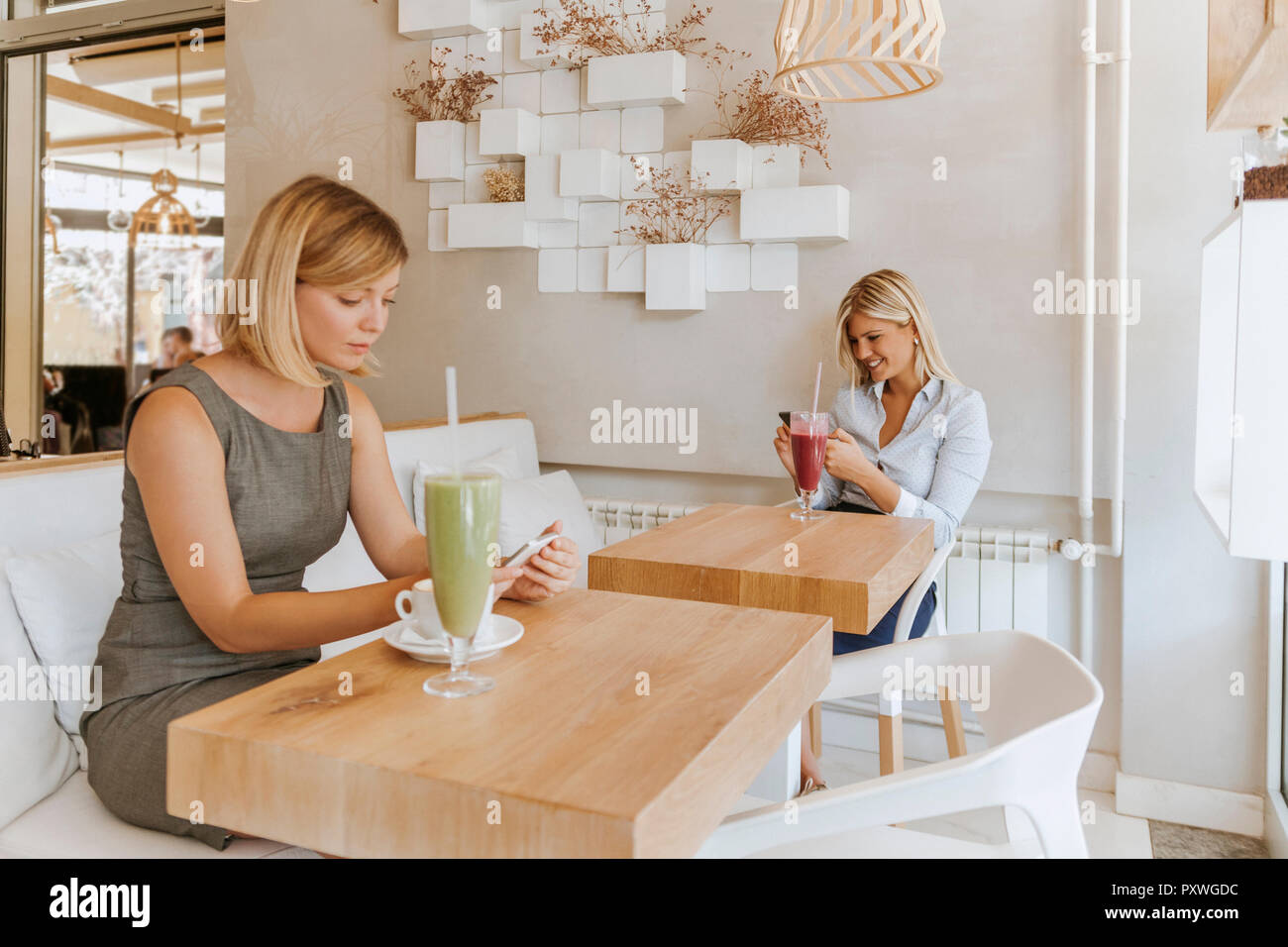 Two young women using smartphones in a cafe Stock Photo