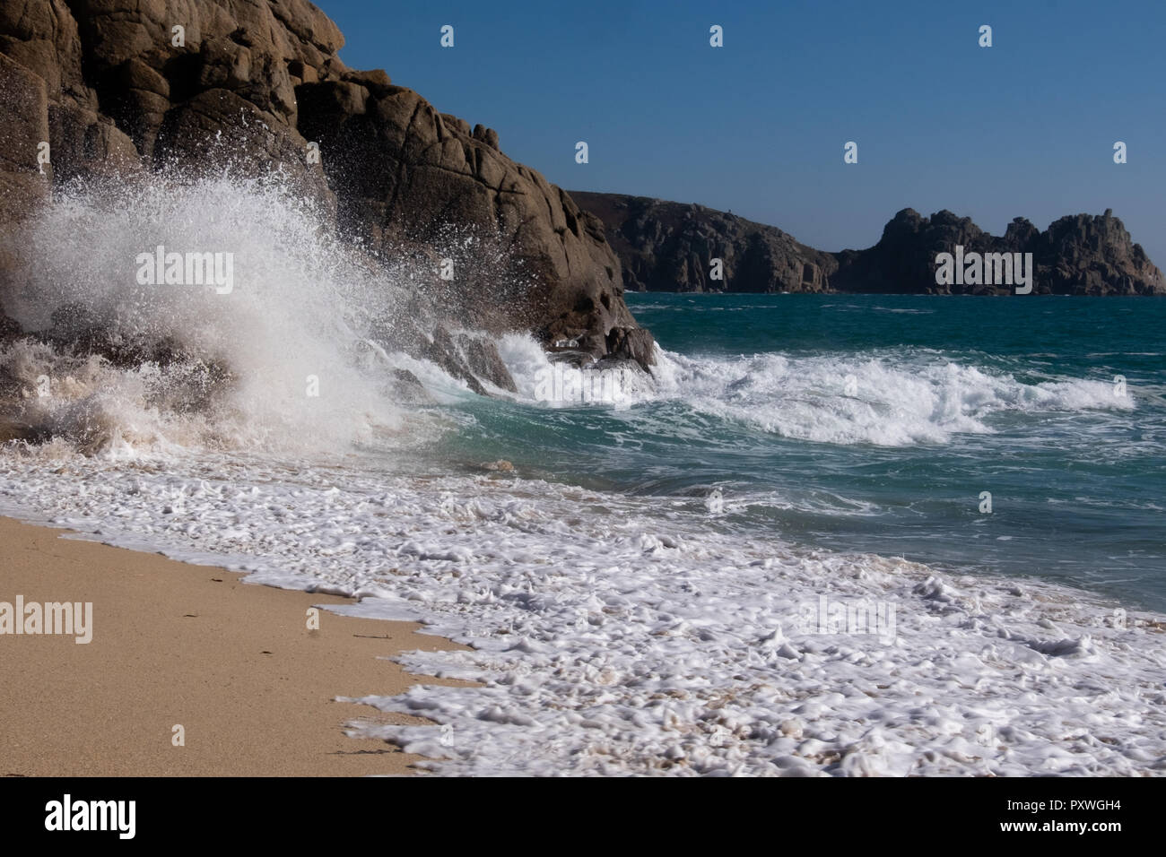 Sea swirling up the beach in waves crashing against the cliff rocks to shower water into the air in a white fountain of power. Stock Photo