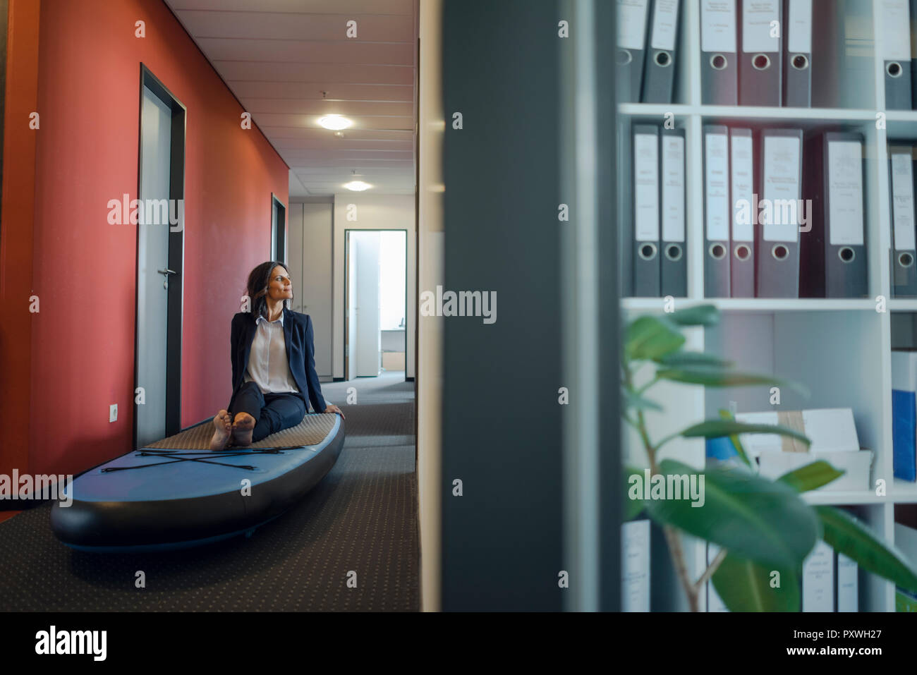 Businesswoman sitting on paddle board, daydreaming in office Stock Photo