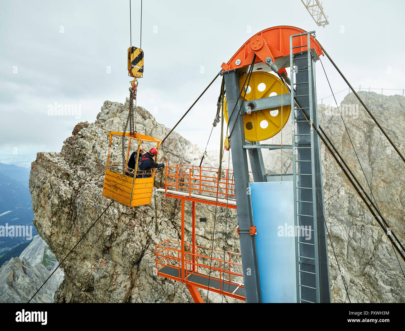 Germany, Bavaria, Garmisch-Partenkirchen, Zugspitze, installers working on goods cable lift in a work cage Stock Photo