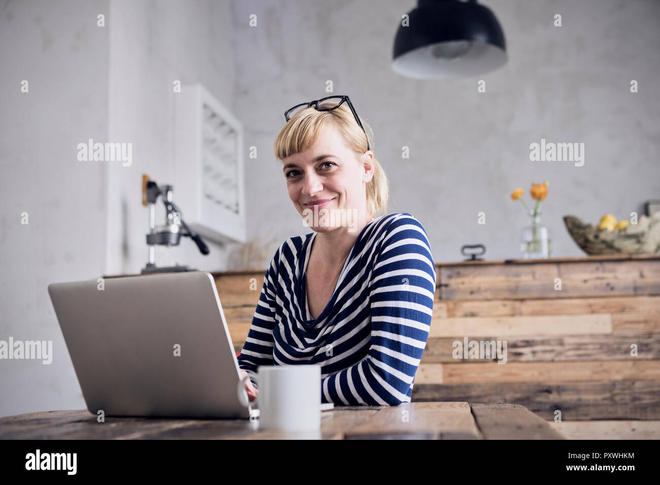 Portrait of smiling woman sitting at table with laptop and coffee mug Stock Photo