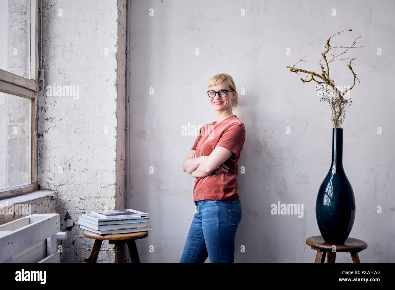 Portrait of smiling woman leaning against wall in loft Stock Photo