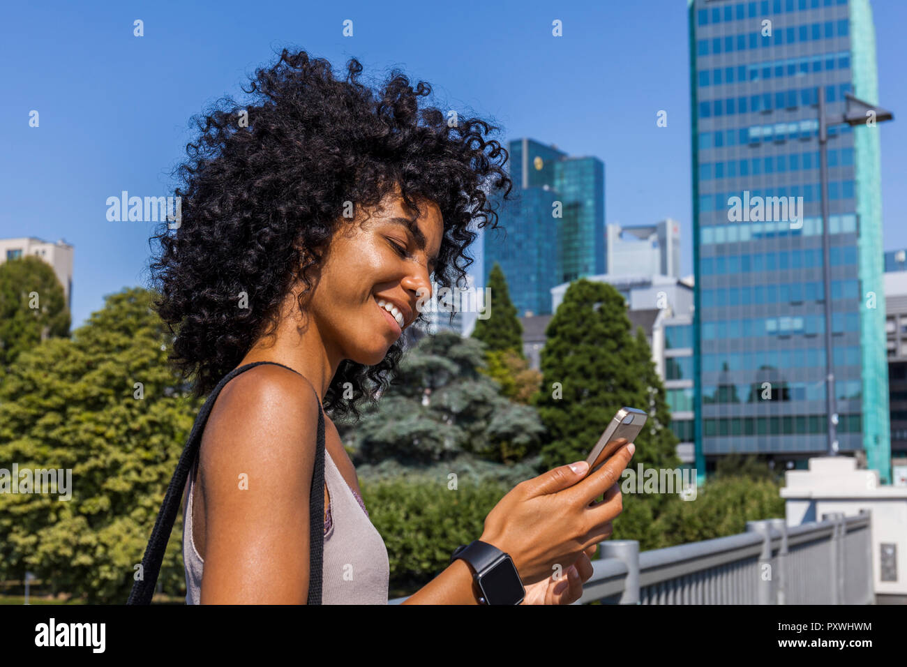 Germany, Frankfurt, smiling young woman with curly hair looking at cell phone Stock Photo