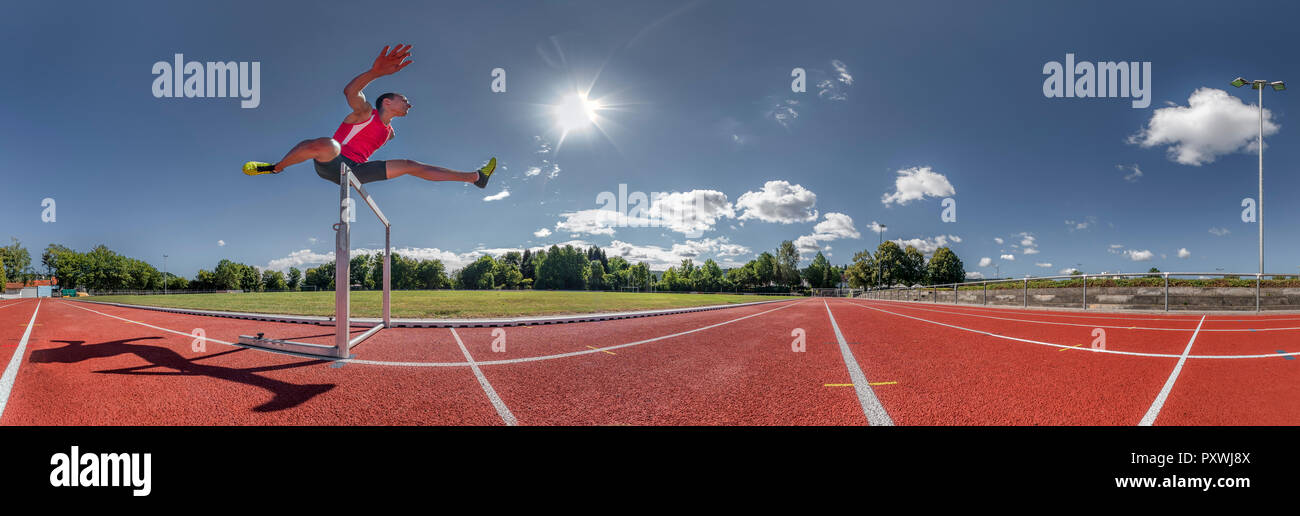 Young runner crossing hurdle, panoramic view Stock Photo