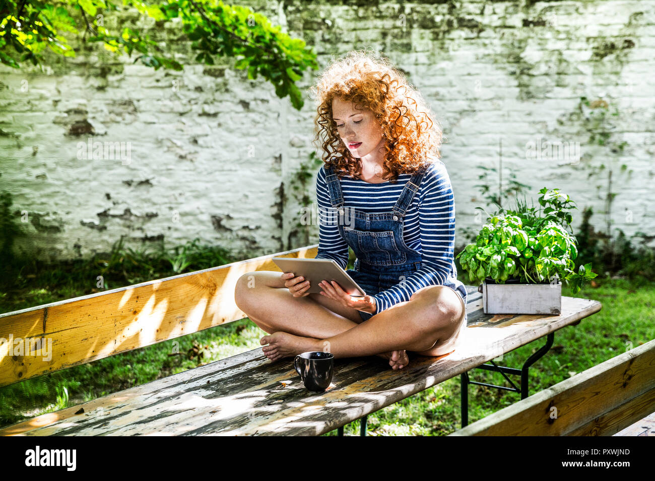 Portrait of young woman sitting on beer table in the garden using tablet Stock Photo