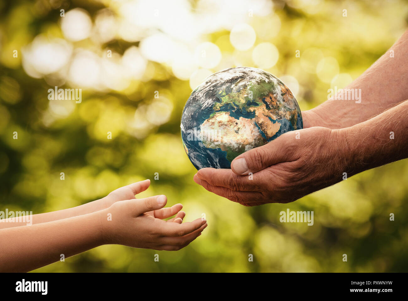 Close up of senior hands giving small planet earth to a child over defocused green background with copy space Stock Photo