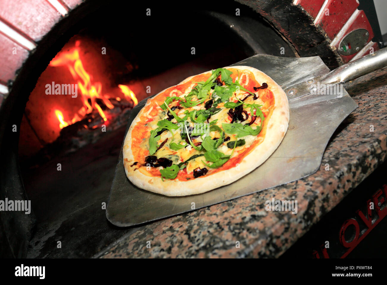 Black Olives, Italian sausage, Ham, fresh Rocket & parmesan shavings Pizza, cooked in a traditional wood fired pizza oven Stock Photo