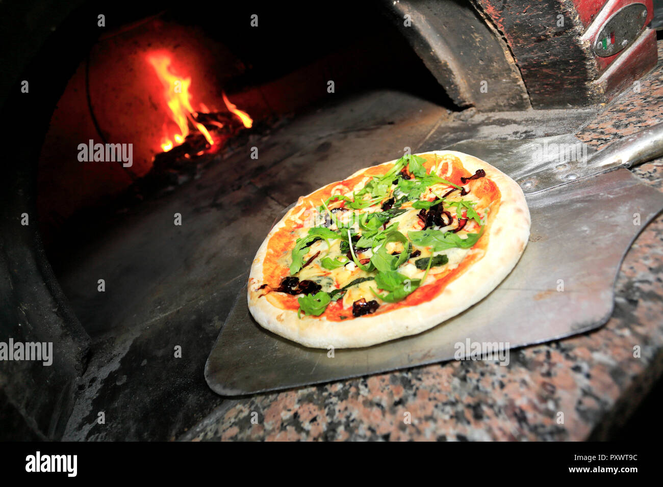 Black Olives, Italian sausage, Ham, fresh Rocket & parmesan shavings Pizza, cooked in a traditional wood fired pizza oven Stock Photo
