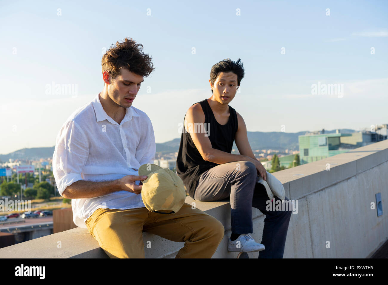 Two young men sitting and talking on a wall Stock Photo