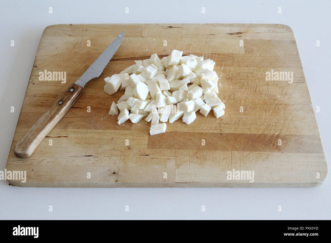 A minced stack of white mozzarella cheese dices on a wooden cutting board with a knife, typical of Italian and Mediterranean cuisine Stock Photo