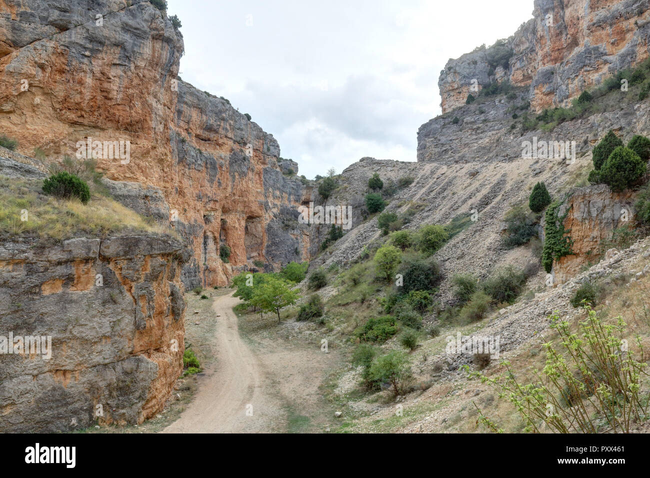 The Barranco de la Hoz Seca (Dry Defile Gully) canyon, with scarps, bushes and red rocks, in a cloudy atumn, in the Jaraba rural town, Aragon, Spain Stock Photo