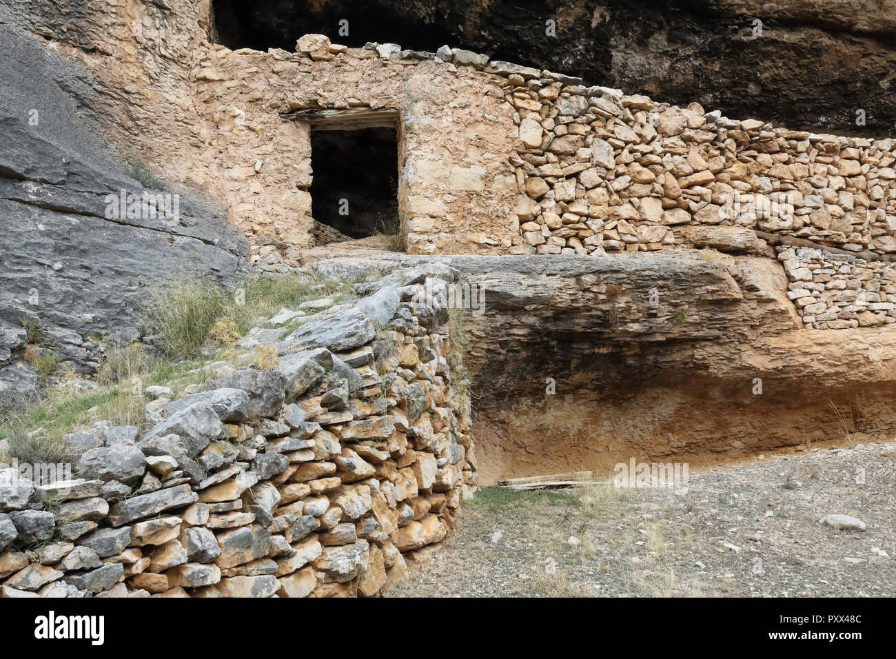 A shelter for shepherds and livestock made of stone drywall inside a cave in the red ferrous rock of the Barranco de la Hoz Seca canyon, Jaraba, Spain Stock Photo