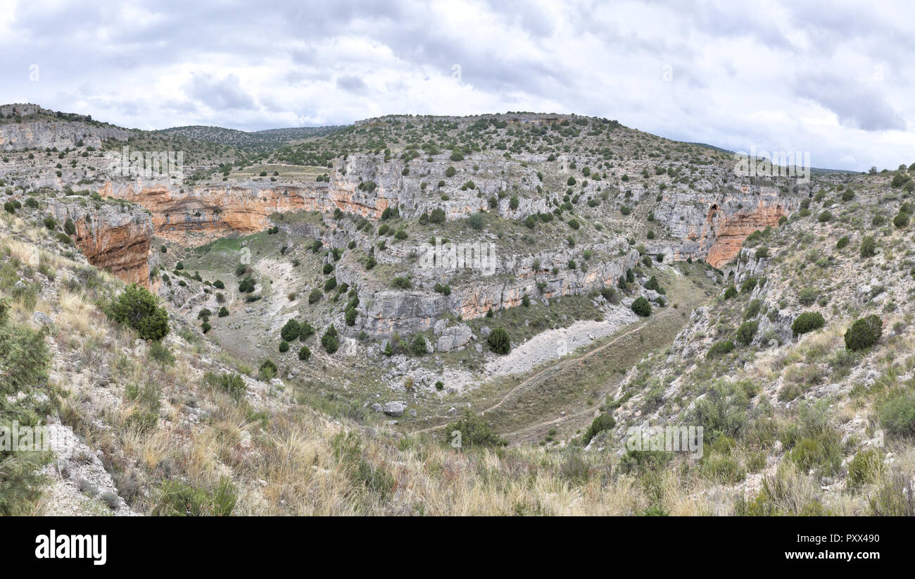 The Barranco de la Hoz Seca (Dry Defile Gully) canyon, with scarps, bushes and red rocks, in a cloudy autumn, in the Jaraba rural town, Aragon, Spain Stock Photo