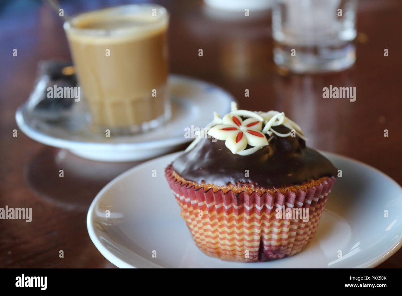 A close view of a chocolate muffin on a plate with a coffe cup on background (cafè con leche) on a table in Zaragoza, Spain Stock Photo