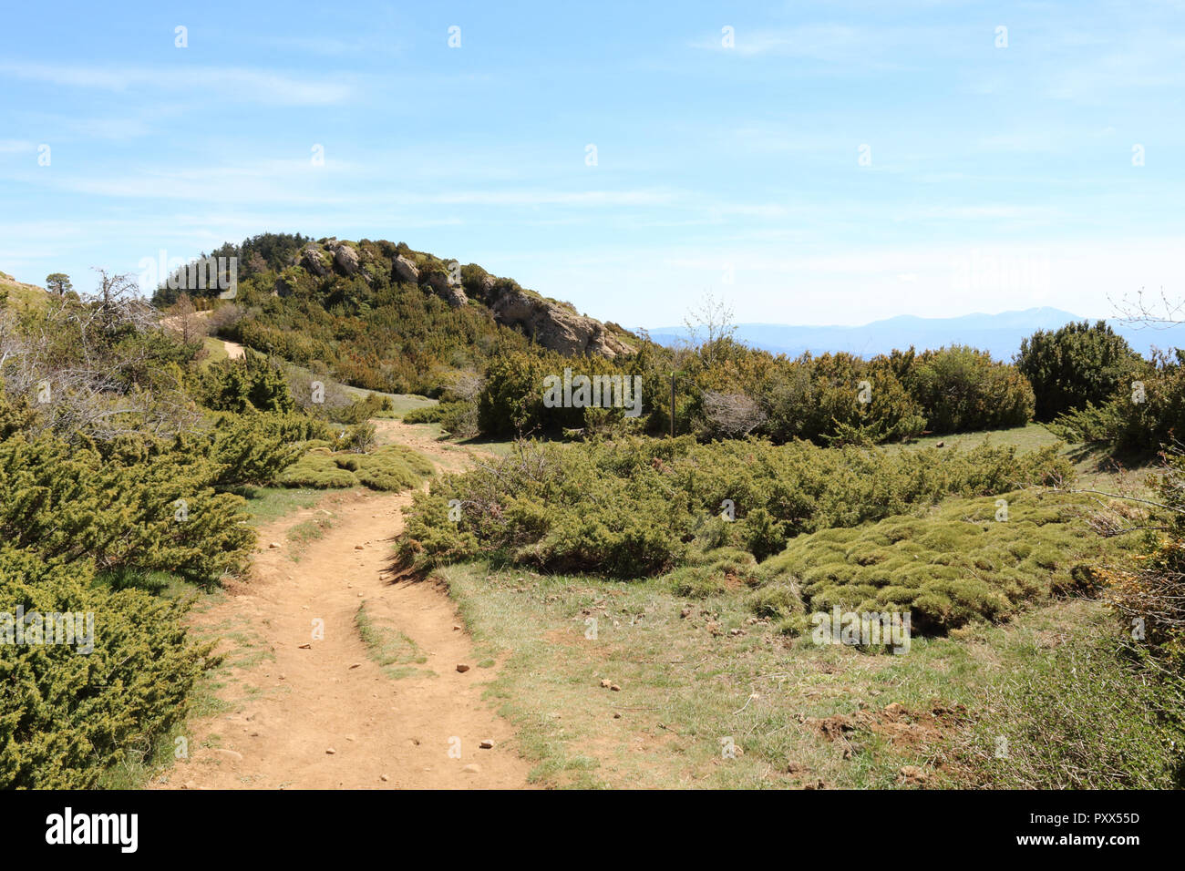 A landscape of a path on the edge of Peña Oroel mount, with the Pyrenees as background, a wide valley with blue sky and some bushes, in Aragon, Spain Stock Photo