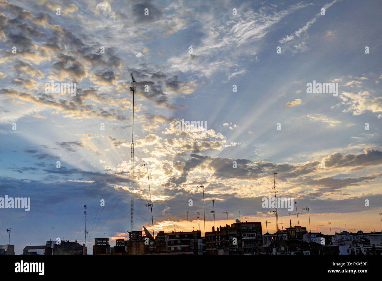 The sunbeams coming out from the pink clouds during an orange dawn on a spring morning, with the city silhouette, in Zaragoza, Spain Stock Photo