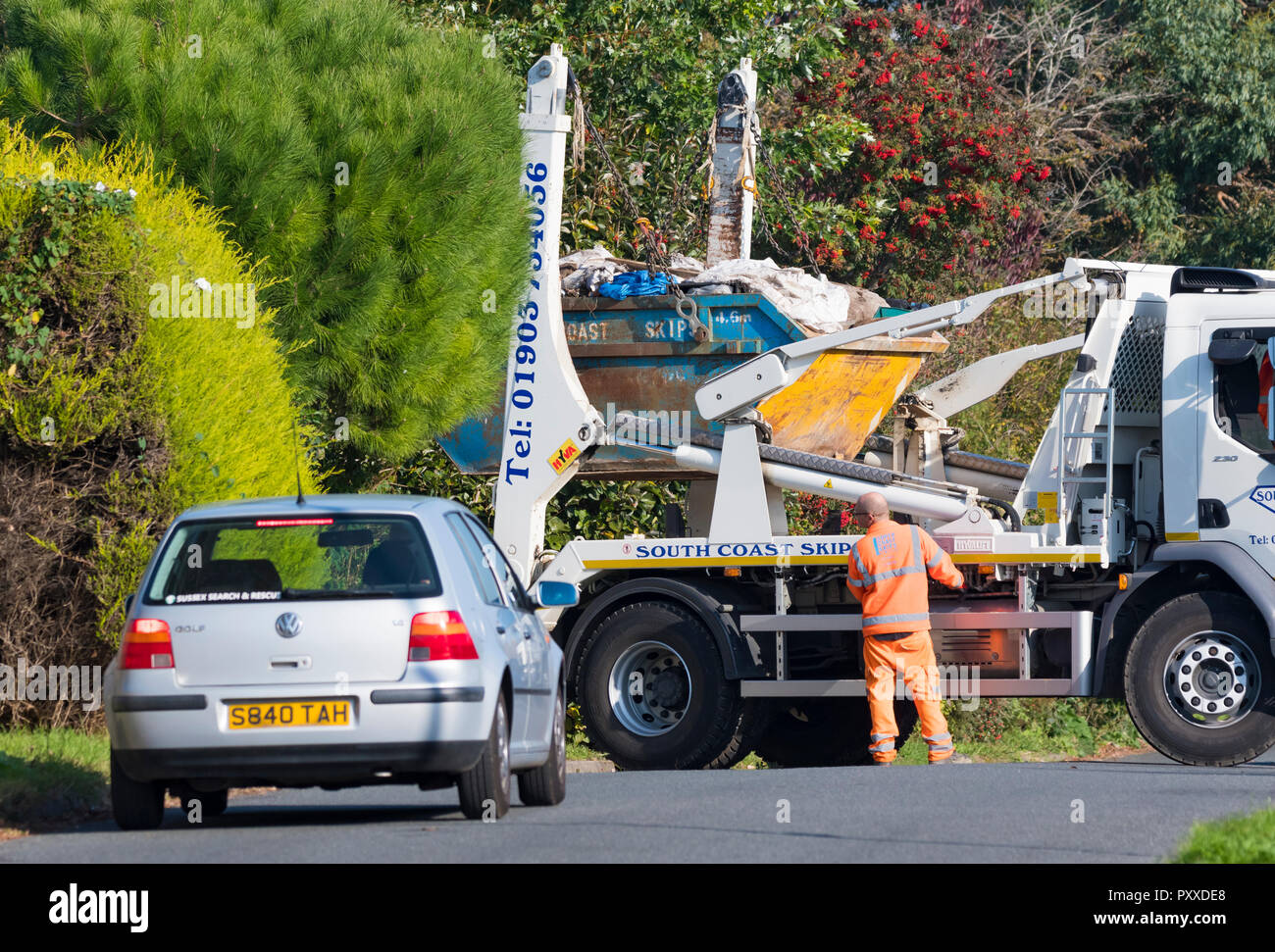 Truck delivering, unloading or picking up a building skip full of building or construction waste from a residential area in the UK. Stock Photo