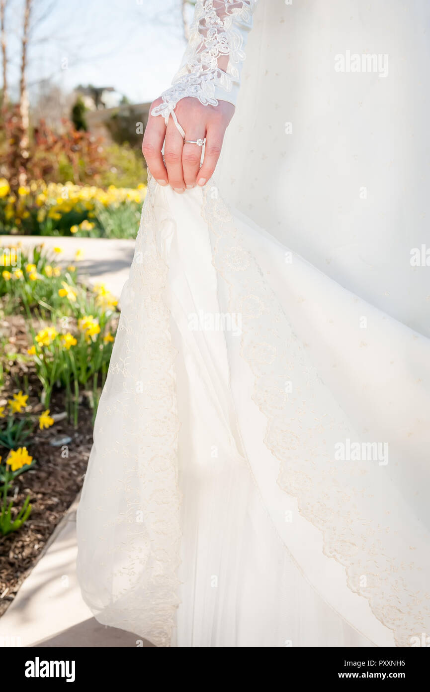 A bride holds up the train of her dress as she walks through a garden of flowers. Stock Photo