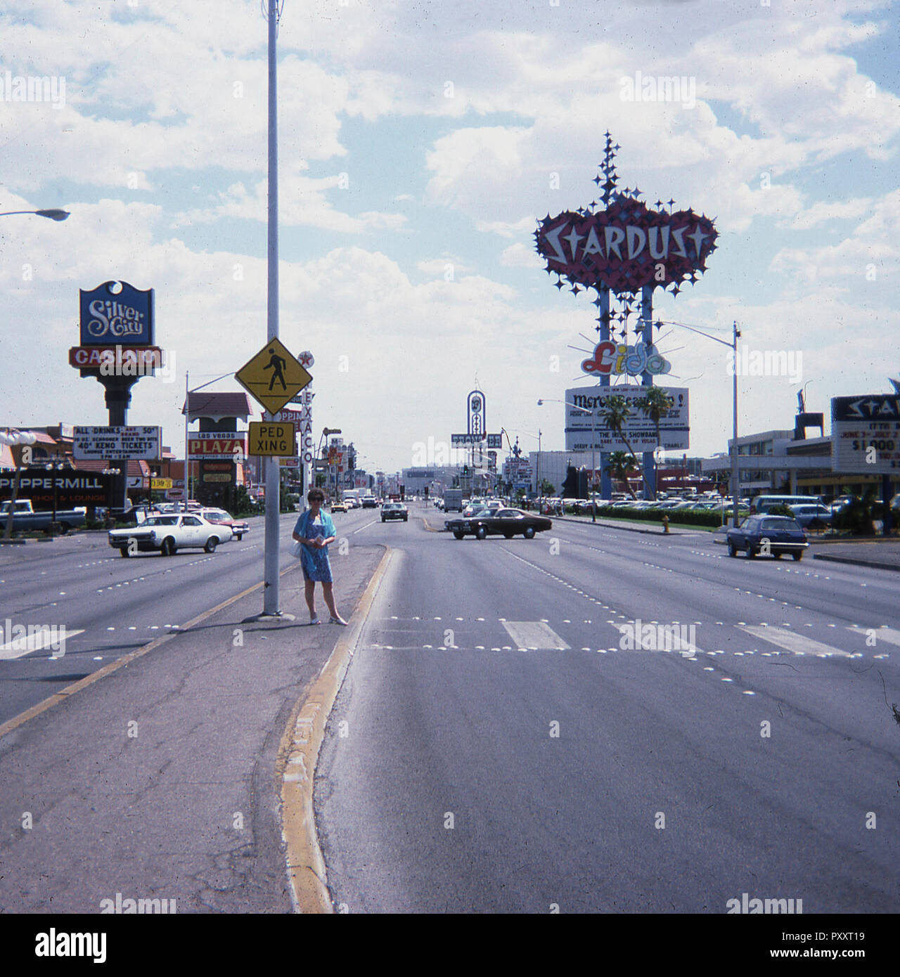 1975, historical, daytime and a lady stands in the middle of 'the strip', a central boulevard in the casino town of Las Vegas, Nevada, USA. A roadside sign (1967) for the 'Stardust', the famous resort hotel and casino which opened in 1958, can be seen in the picture and was made up of a scatter of neon star shapes which lit up at night. Stock Photo
