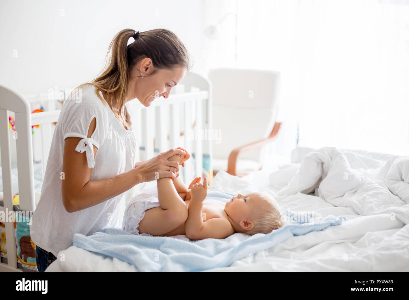 Young mom, changing baby diaper after bath in sunny bedroom Stock Photo