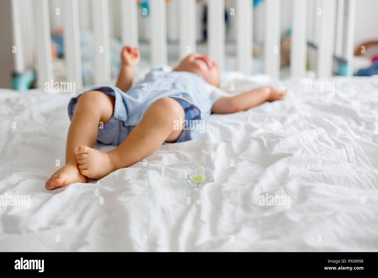 Toddler baby boy, playing with dummy, crying unhappy for the pacifier in children bedroom Stock Photo