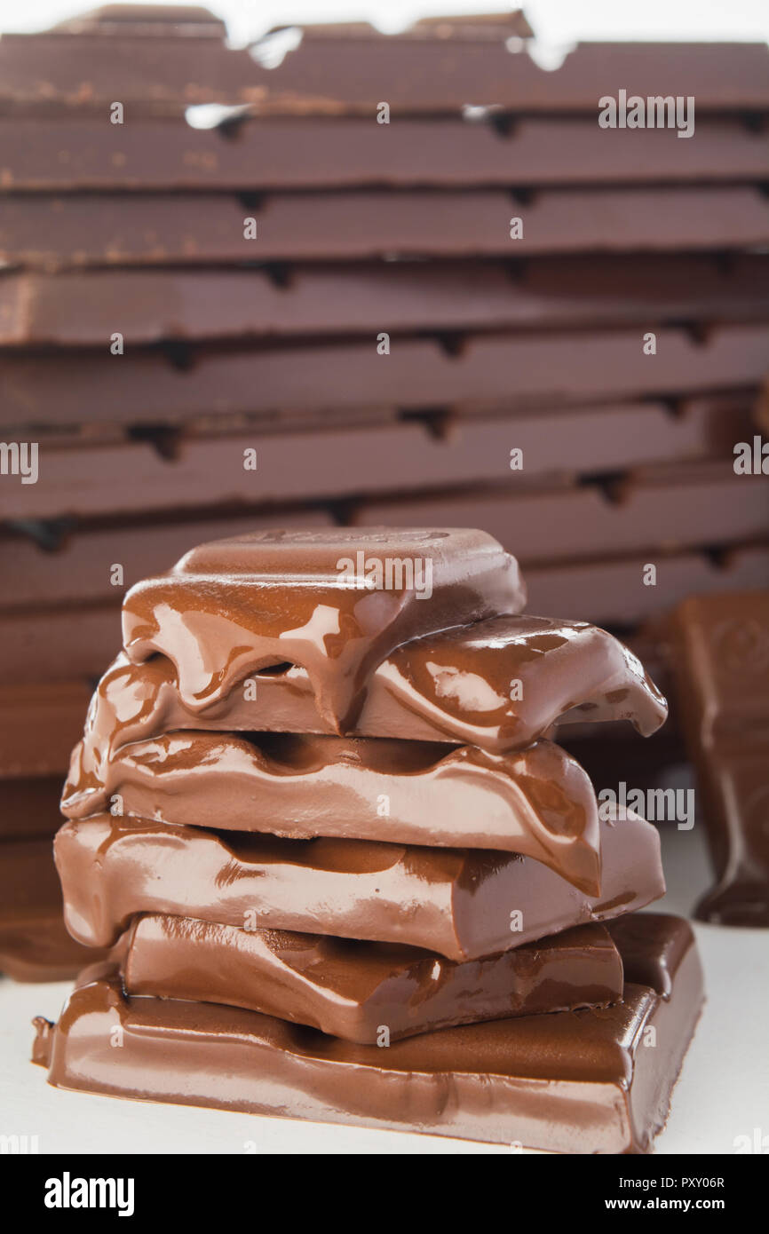 Stack of melting chocolate's pieces with big stack of chocolate on background, vertical shot Stock Photo