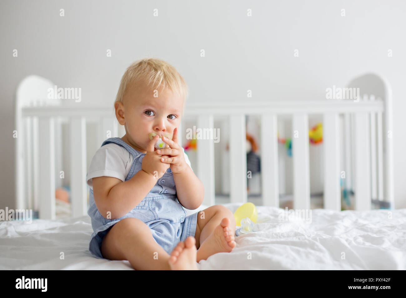 Toddler baby boy, playing with dummy, crying unhappy for the pacifier in children bedroom Stock Photo