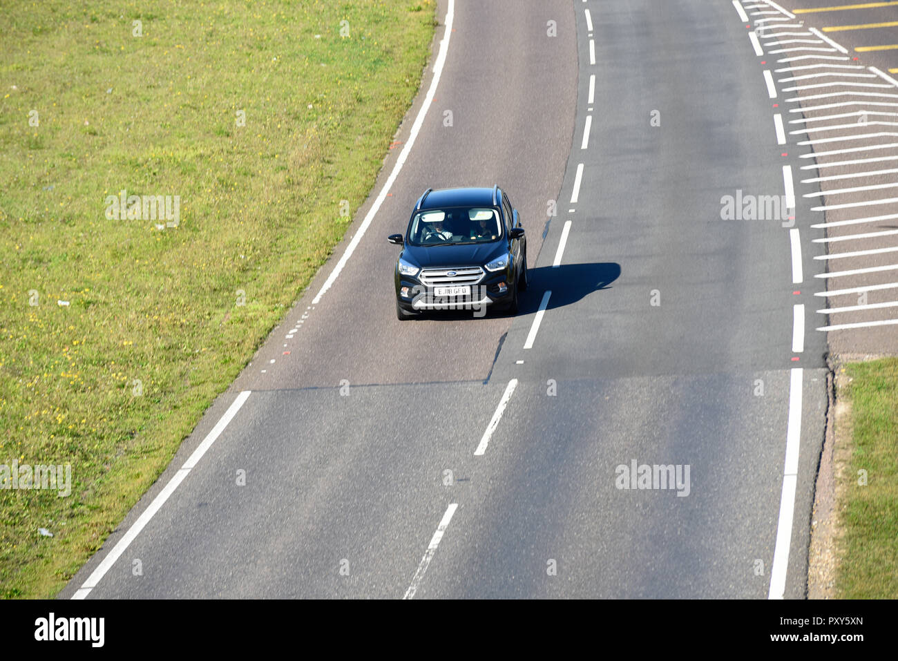 Lone car driving on a stretch of A130 duel carriageway after exit. Ford Kuga. Single vehicle automobile on road Patchwork road surfaces Copyspace Stock Photo