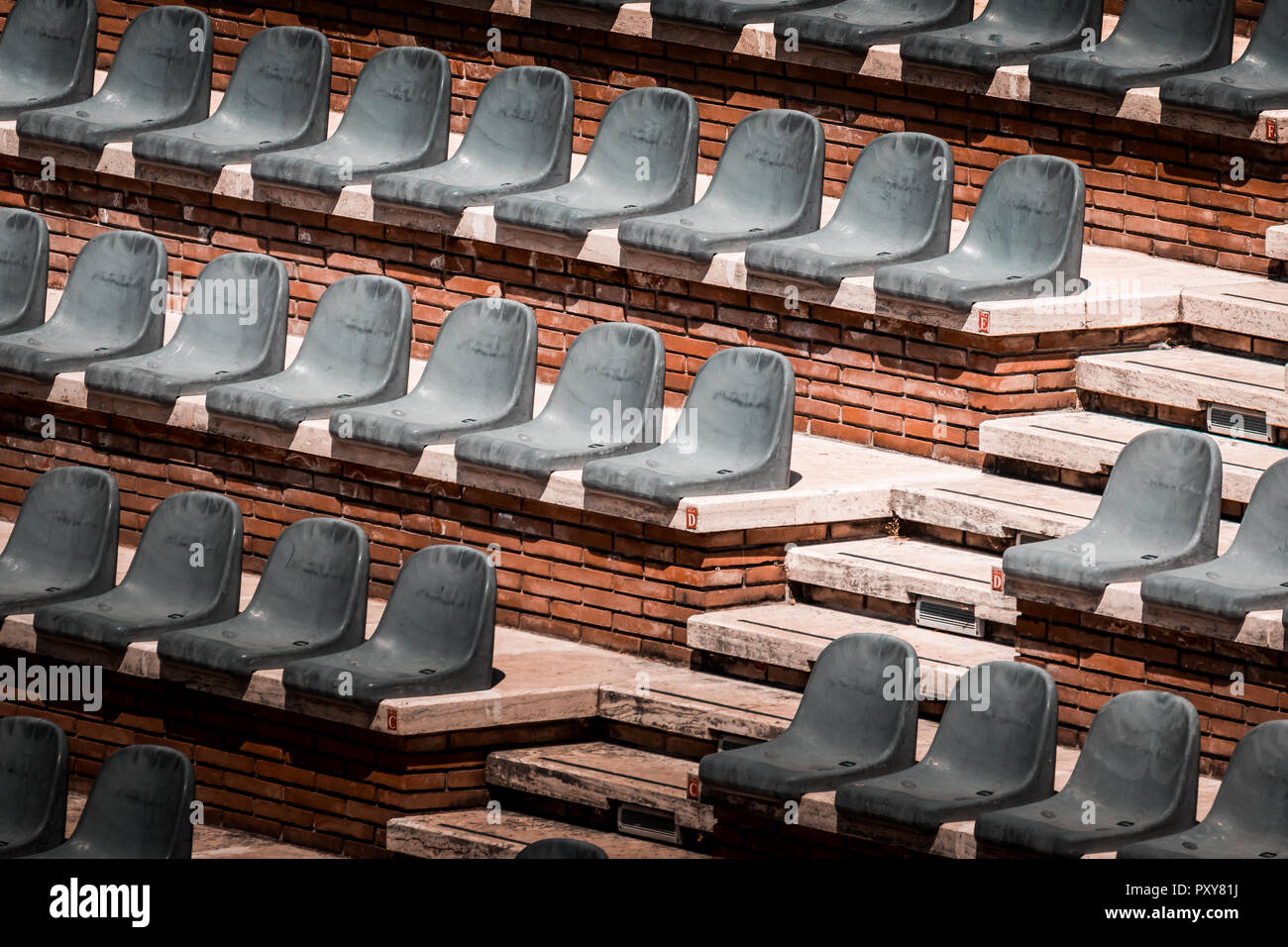 Free unclaimed seats in multiple rows. Sunset photo in empty public arena and concert amphitheatre. Red brick and white travertine structure. Stock Photo