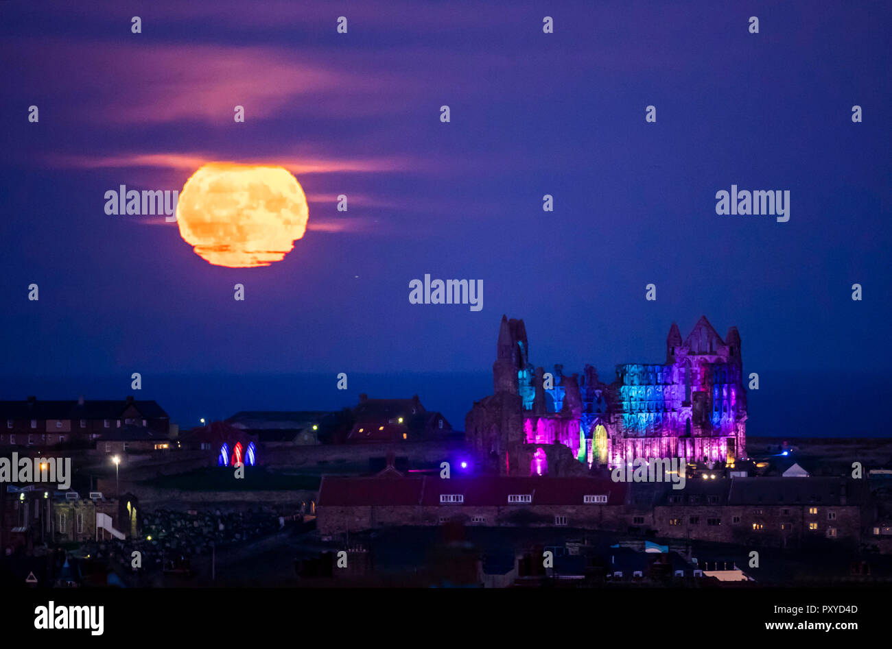 A Hunter's Moon rises over the illuminated ruins of Whitby Abbey in North Yorkshire. Stock Photo