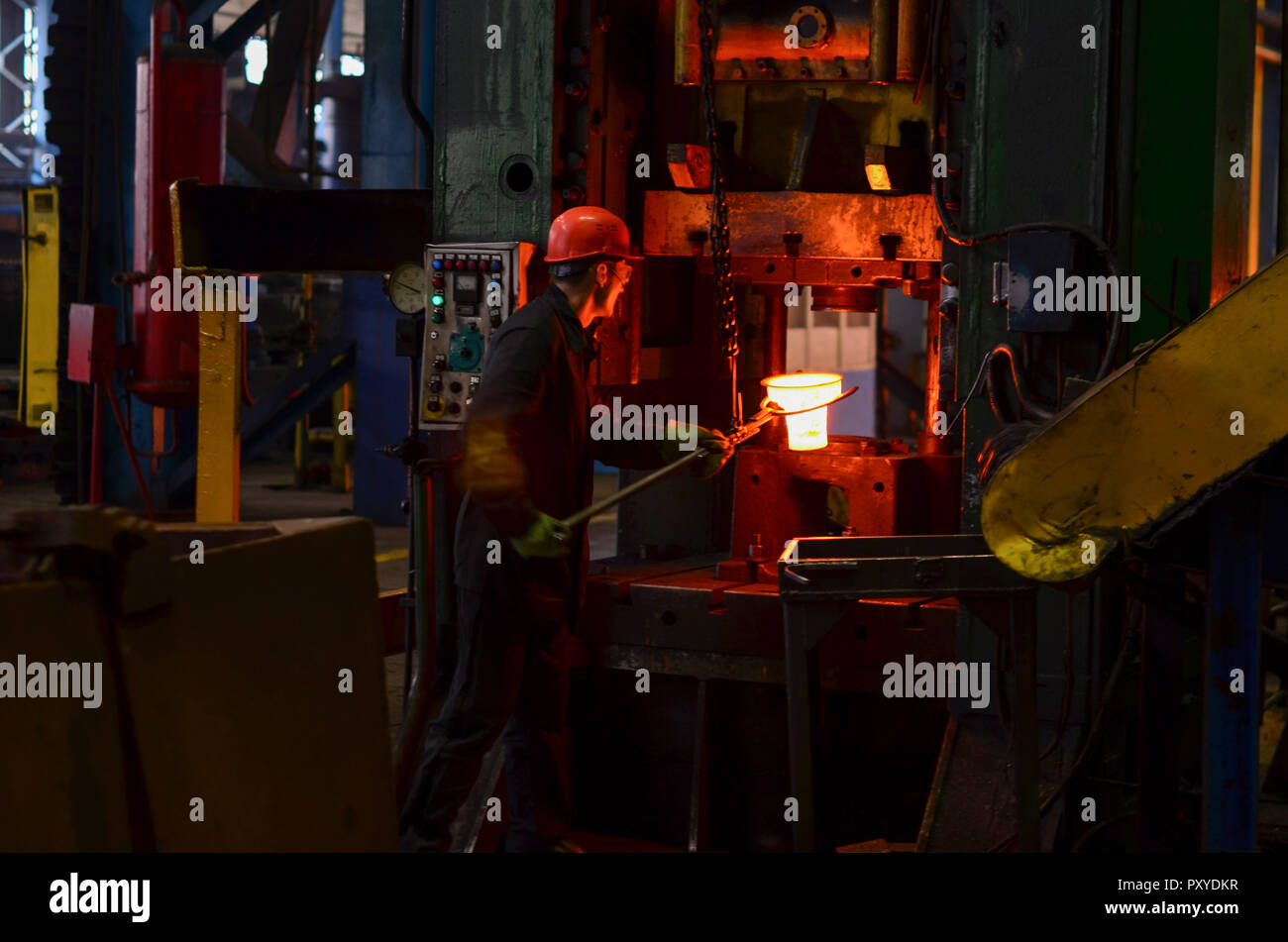 Hot metal ingot being loaded into a hammer forge. Worker forges iron products Stock Photo