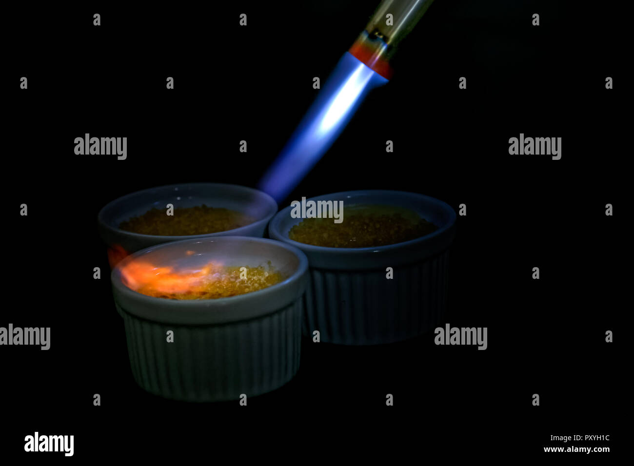 Blow torch caramelizing ramekin of creme brulee. Isolated on black