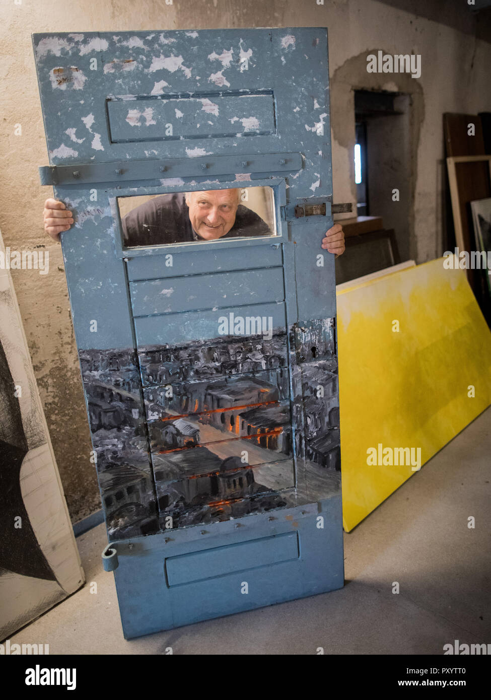 Kaarst, Germany. 23rd Oct, 2018. Helge Achenbach, former art consultant, looks at the Kunsthof through a discarded prison door on which a depiction of the destroyed Syrian city of Aleppo is painted. Achenbach is committed to politically persecuted artists on the former farm on the Lower Rhine. Once an art consultant to the rich and beautiful, Achenbach had betrayed Berthold Albrecht, the Aldi heir who died in 2012, when he bought art and vintage cars at hidden surcharges, and had been sentenced to six years in prison. (to dpa-KORR of 25.10.2018) Credit: Rolf Vennenbernd/dpa/Alamy Live News Stock Photo